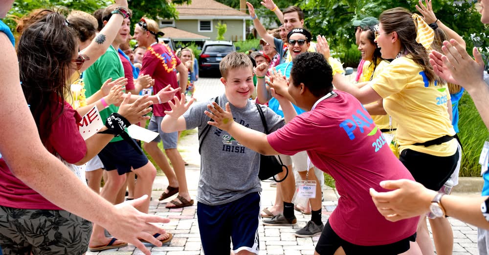 Image of a group of people from PALS forming two rows and high fiving the people walking in the middle through a pathway,